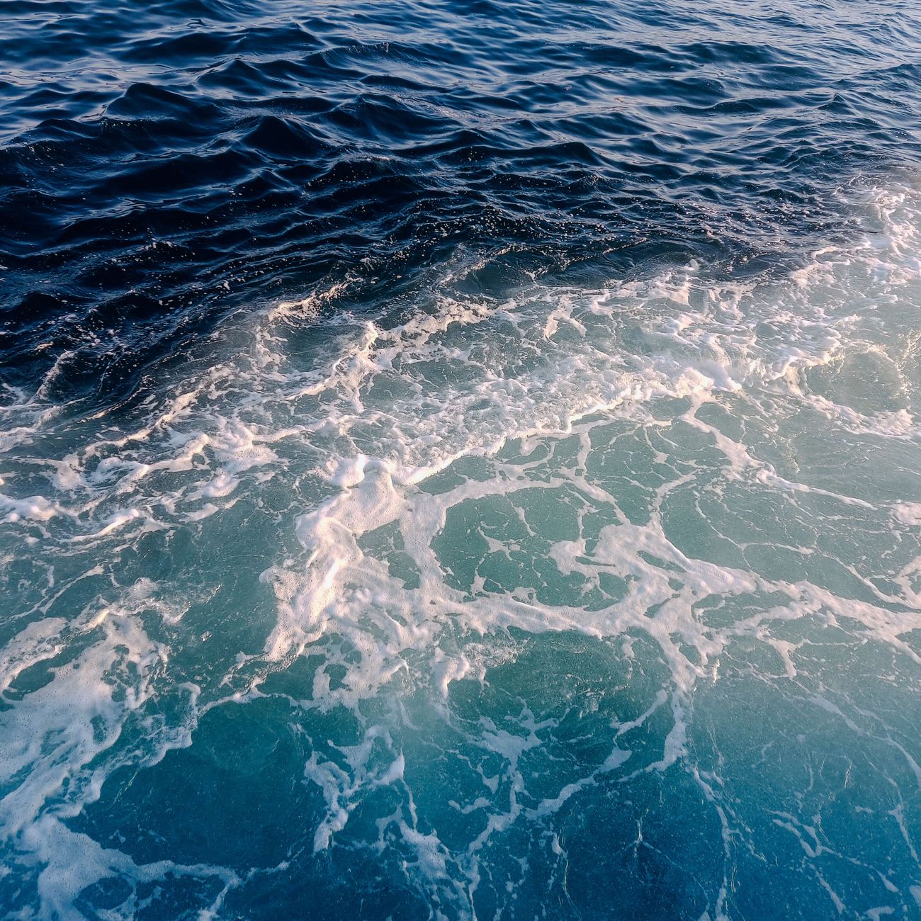 Dynamic top view of turquoise ocean waves forming foamy patterns.