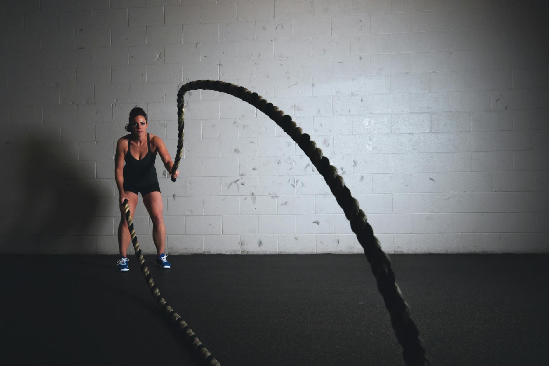 A focused woman performs a dynamic battle rope exercise in a gym setting, demonstrating strength and fitness.