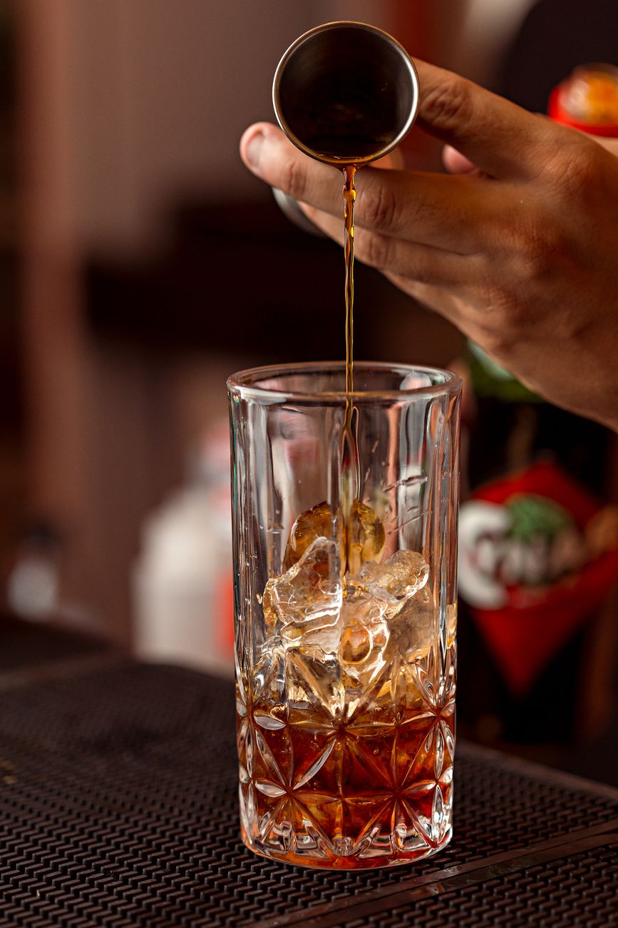 Close-up of a bartender's hand skillfully pouring a cocktail with ice cubes using a jigger.