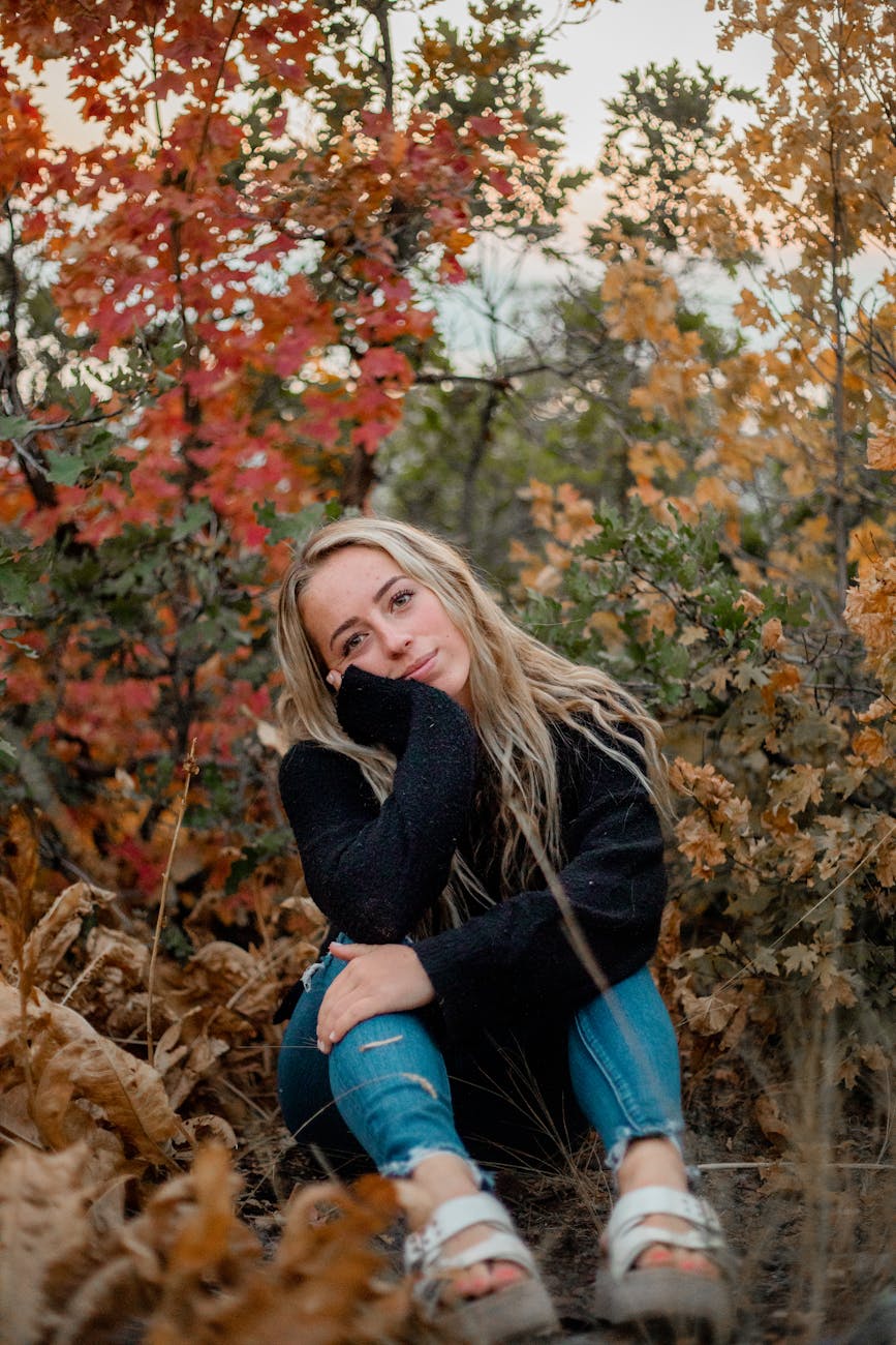 Portrait of a smiling woman sitting among colorful autumn leaves in a tranquil park.