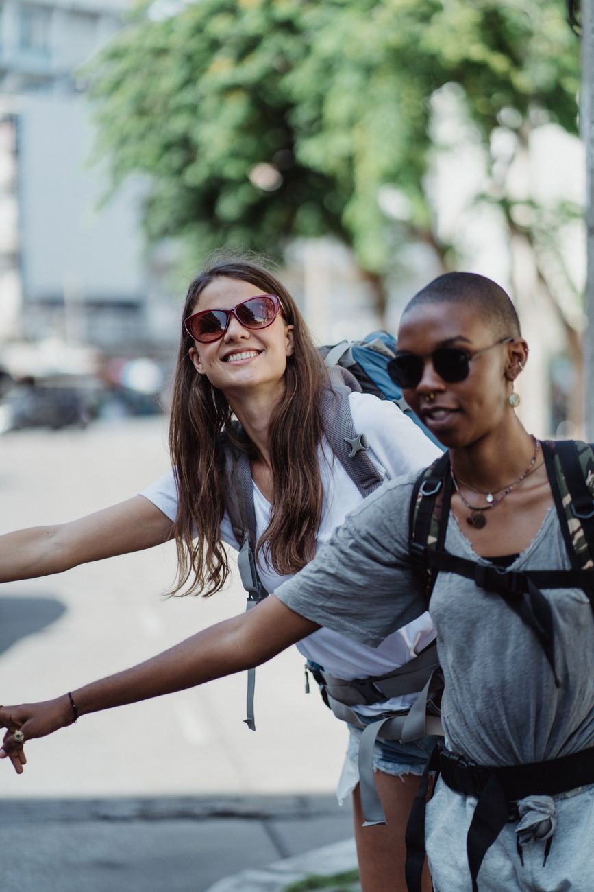 Two young women hitchhiking in an urban setting, embracing travel and adventure.