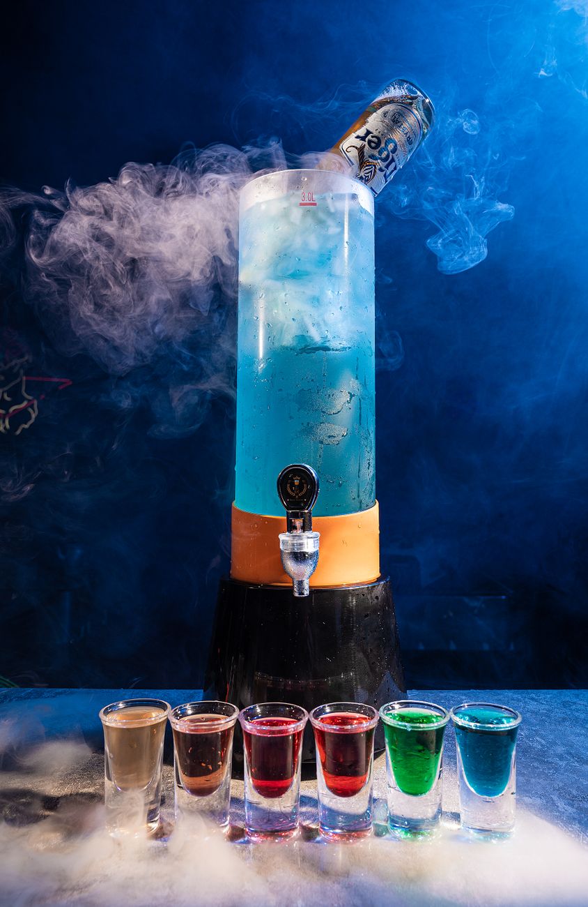 Vibrant cocktail tower with vapor and colorful shots lined up against a blue background.