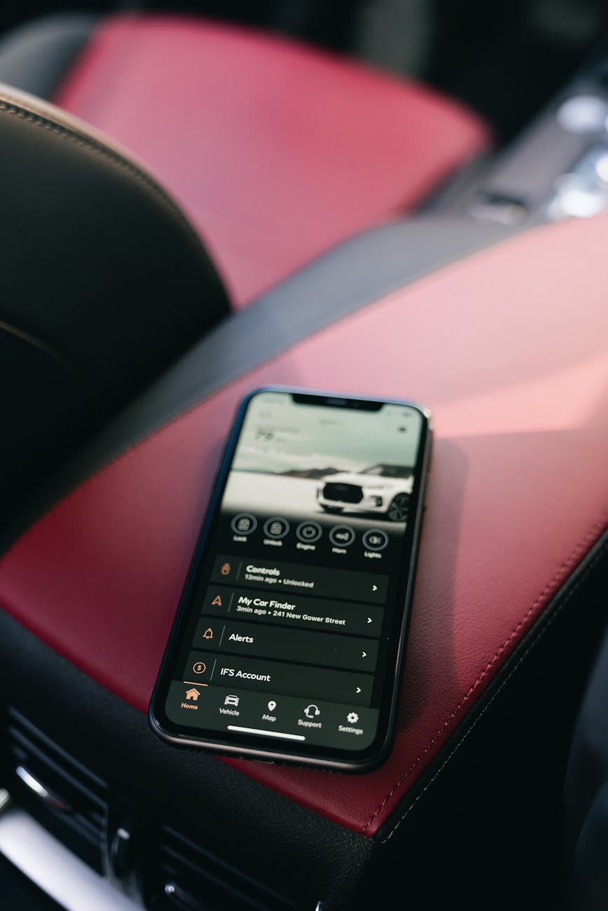 Smartphone displaying car app on red leather car console, interior view.