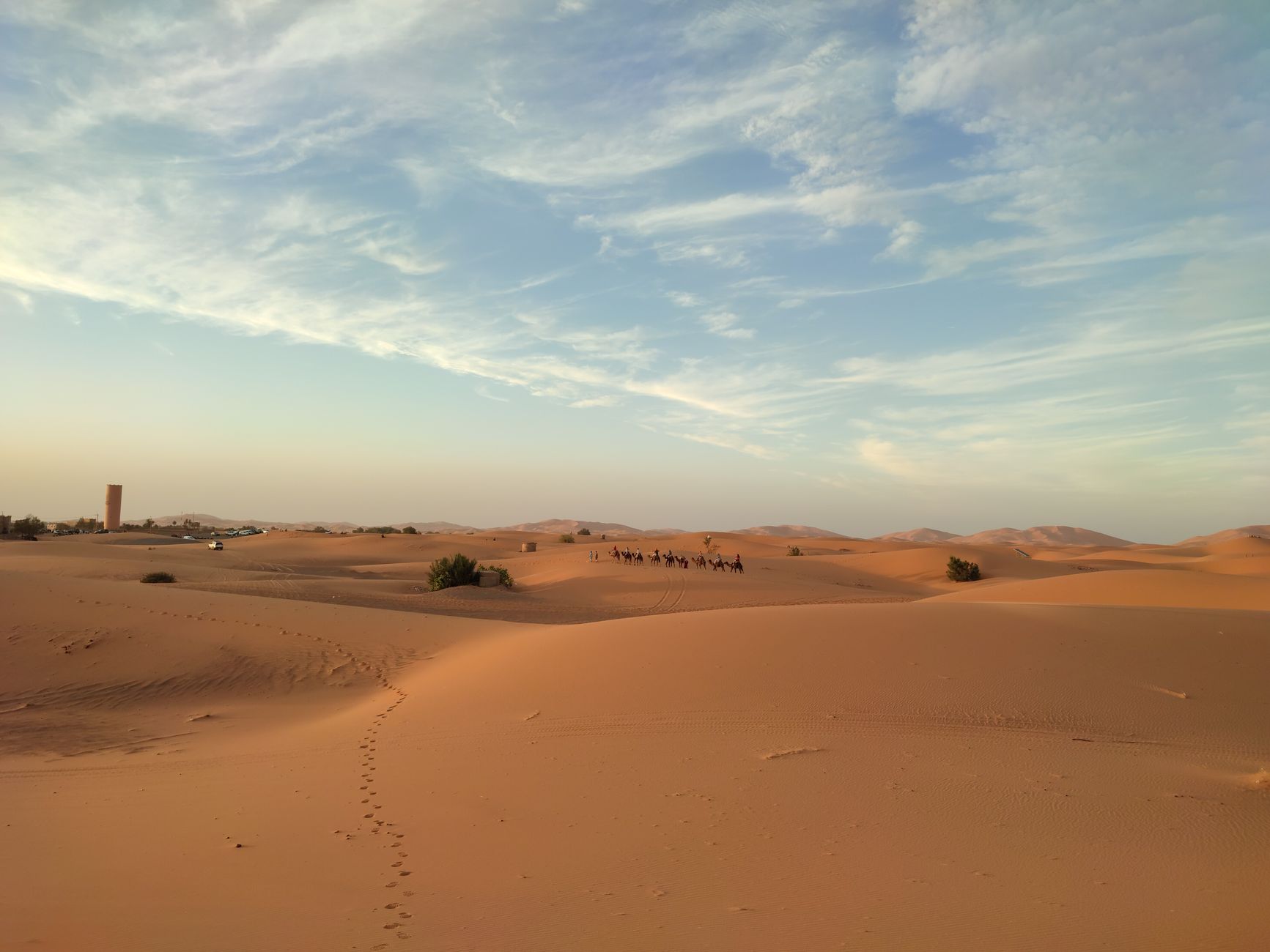 A beautiful desert scene featuring a caravan of camels traveling across sand dunes under a vast sky.