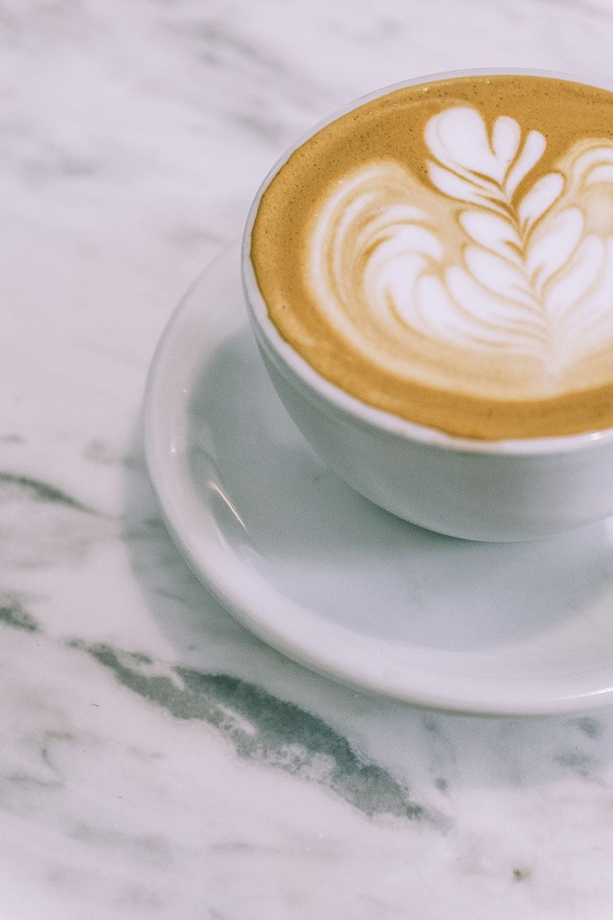 From above cup of appetizing hot foamy cappuccino with latte art placed on marble table in cafe