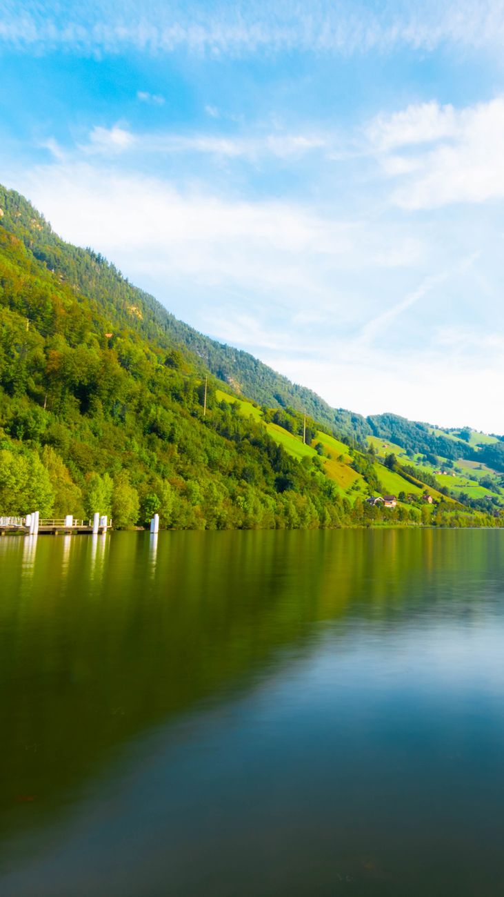 Idyllic view of Alpnachstad lake with lush green hills reflecting in the water under a bright sky.