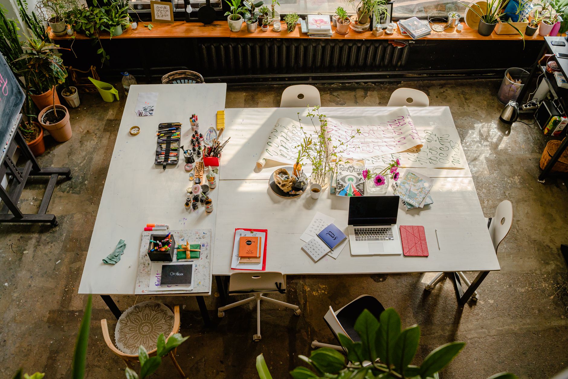 Aerial view of a bright, creative workspace featuring art supplies, plants, and a laptop.