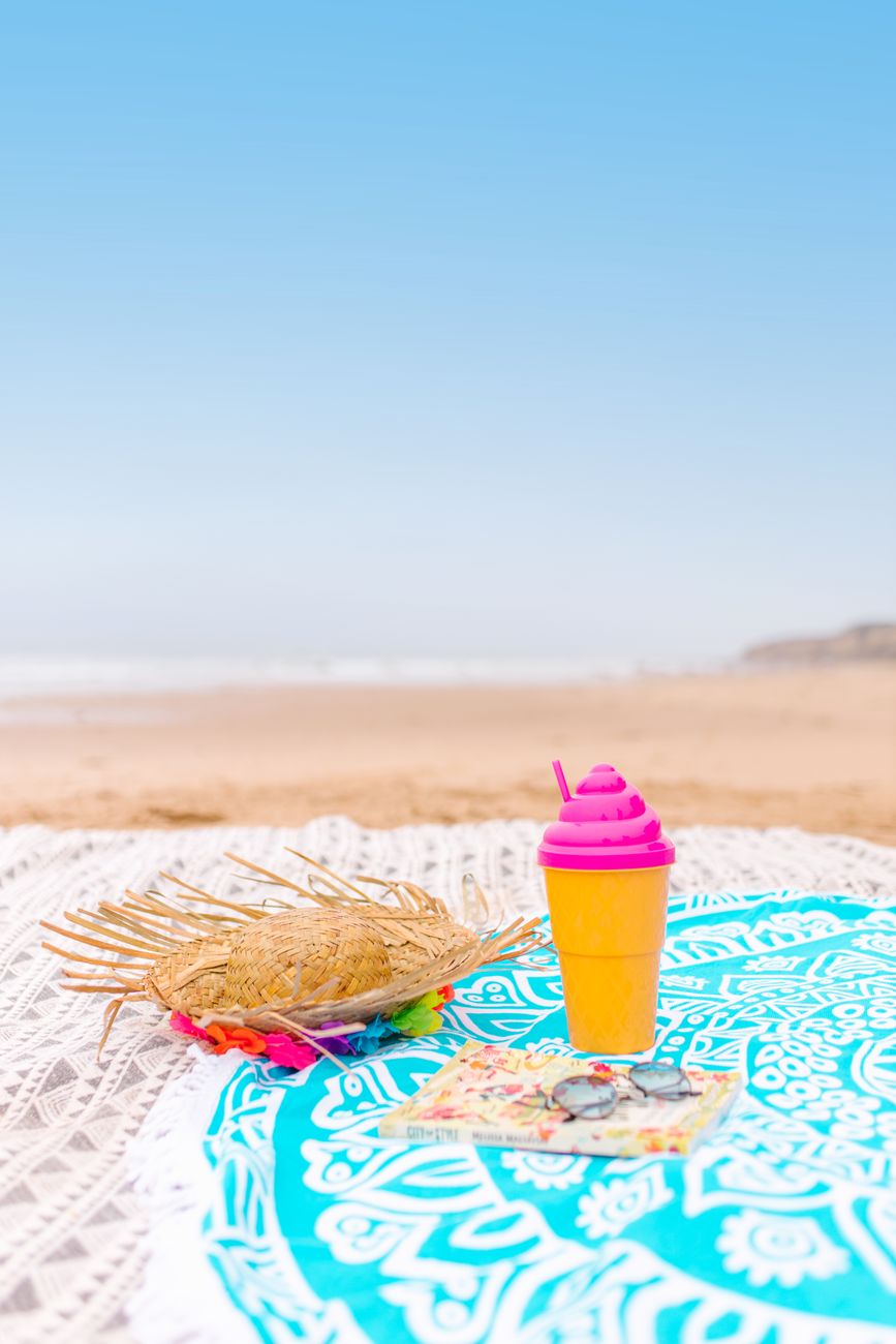 Vibrant summer scene with sun hat, drink, and book on a beach.