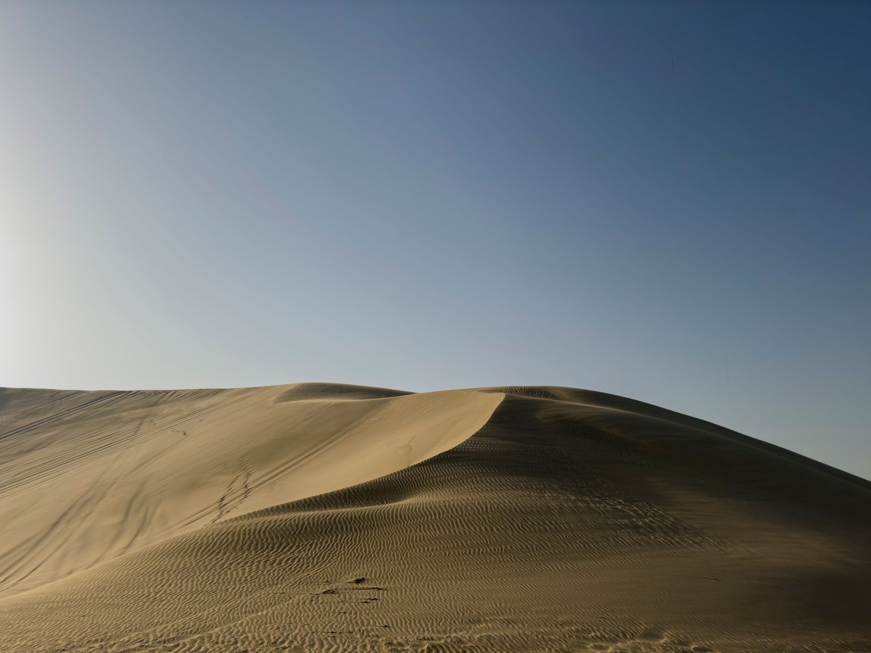 A breathtaking view of golden sand dunes under a clear blue sky in a tranquil desert landscape.