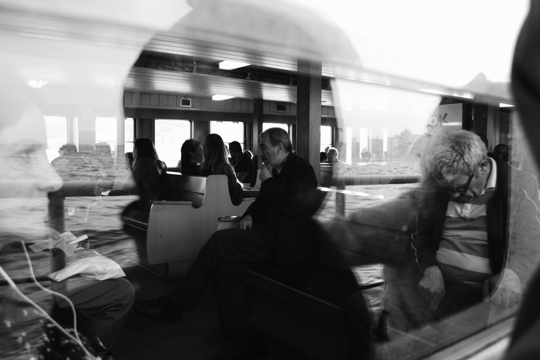 Black and white photo capturing introspective ferry passengers through glass reflections.