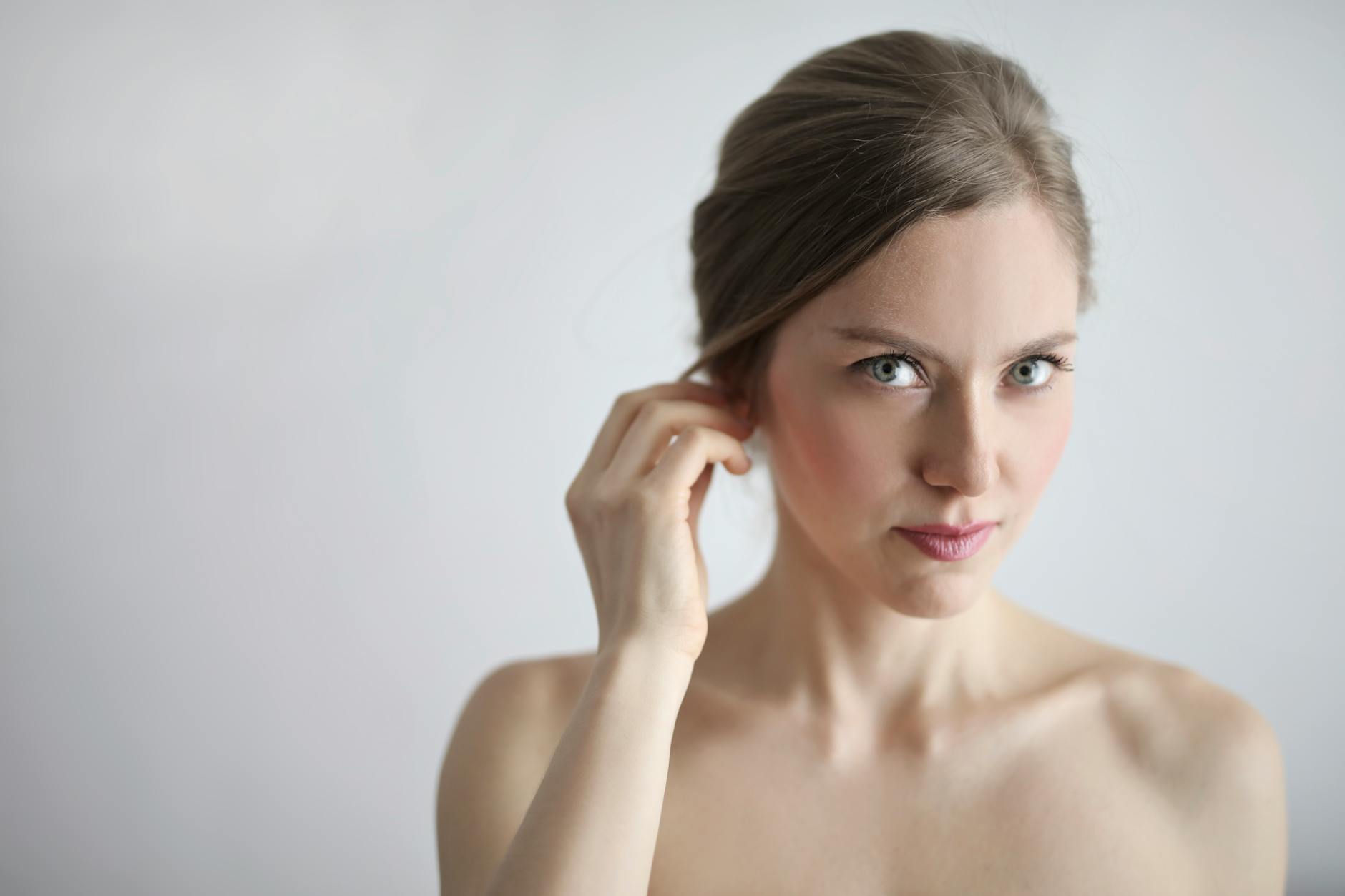 Close-up portrait of a young woman with natural makeup, showcasing elegance and beauty with a soft white background.