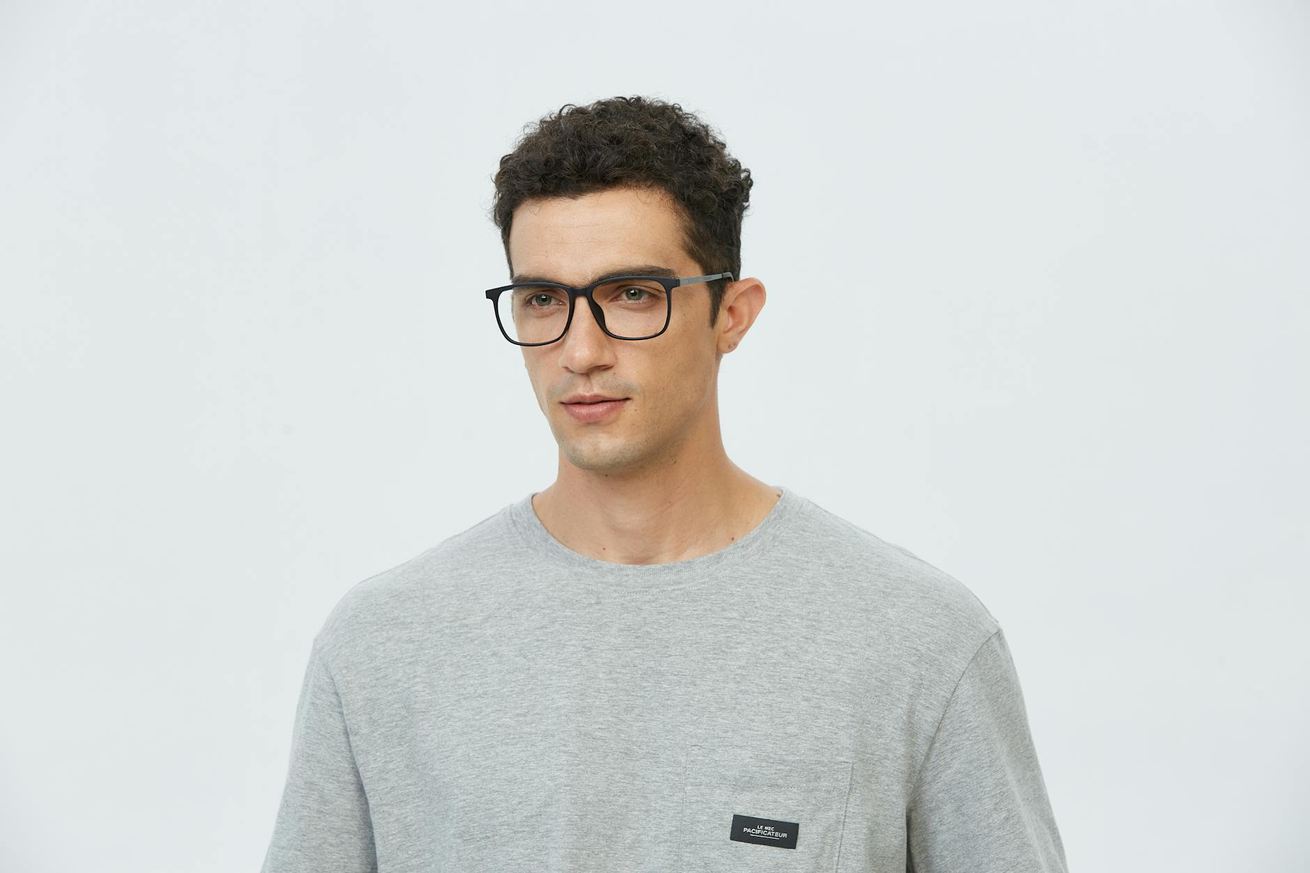 Portrait of a young man wearing glasses in a casual gray t-shirt, looking pensive.