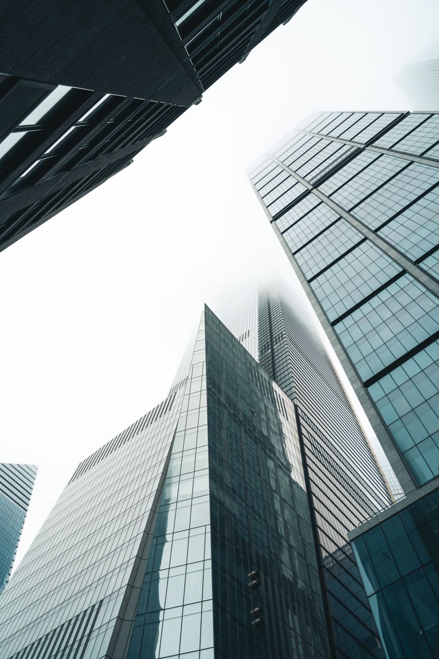 Low-angle view of modern skyscrapers towering into a foggy sky, illustrating urban architecture.