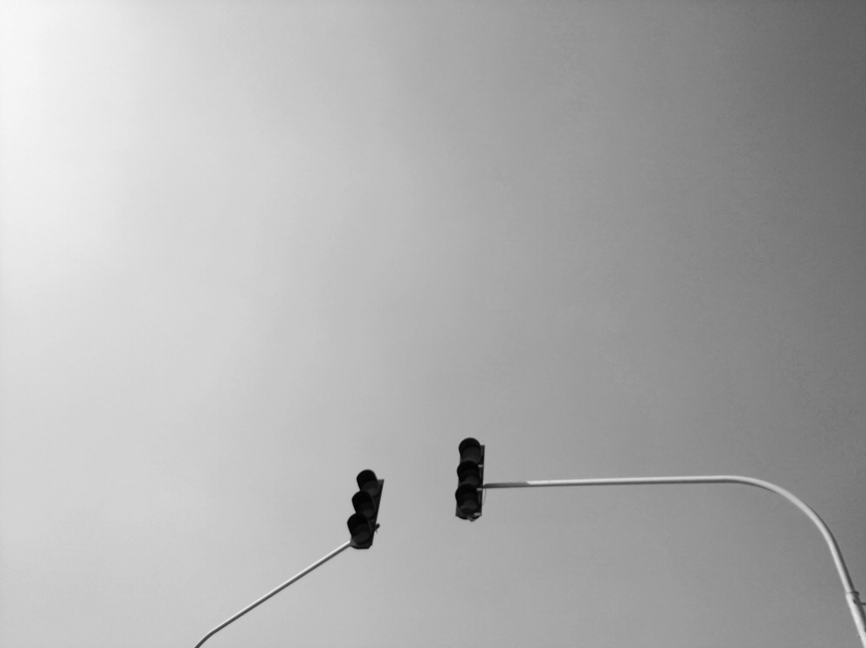 A minimalist black and white photograph of traffic lights against a blank sky in Kahramanmaraş, Turkey.