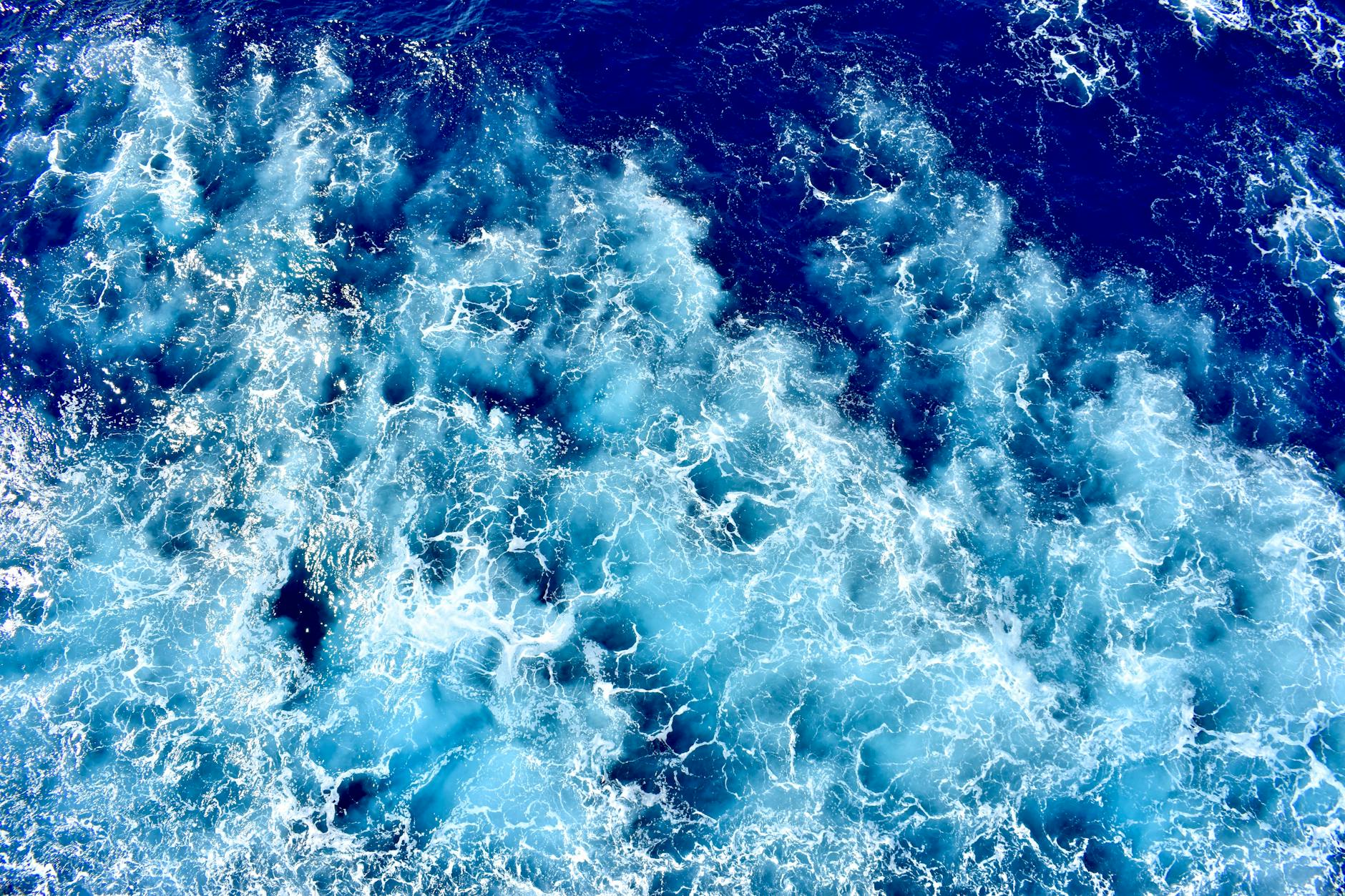 Dynamic aerial perspective of vibrant blue waves crashing in the ocean, exhibiting movement and energy.