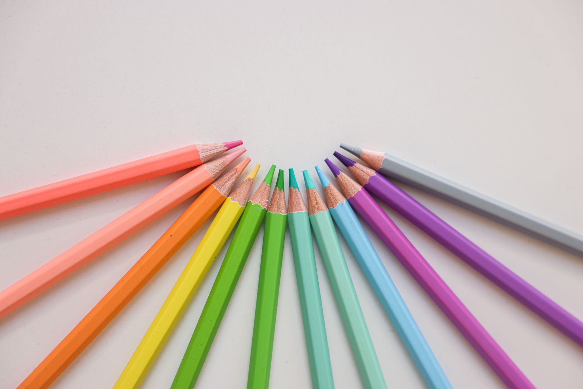 Colorful arrangement of colored pencils on a white surface forming a semicircle.